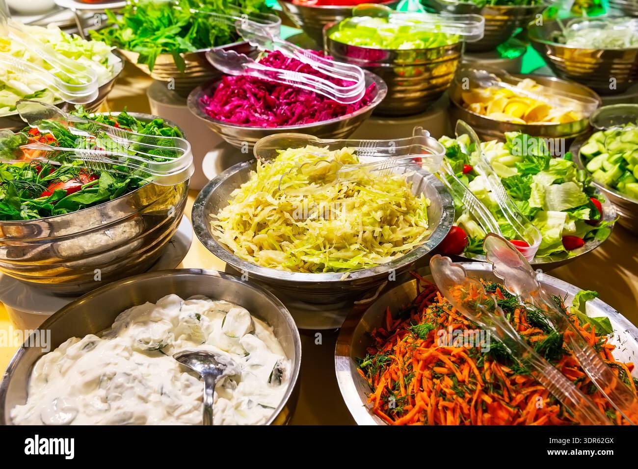 Eine bunte Auswahl an frischen Gemüsesalaten, einschließlich Tomaten, Gurken, Karotten und Kohl, sind in Salatschalen auf dem Buffettisch angeordnet. Stockfoto