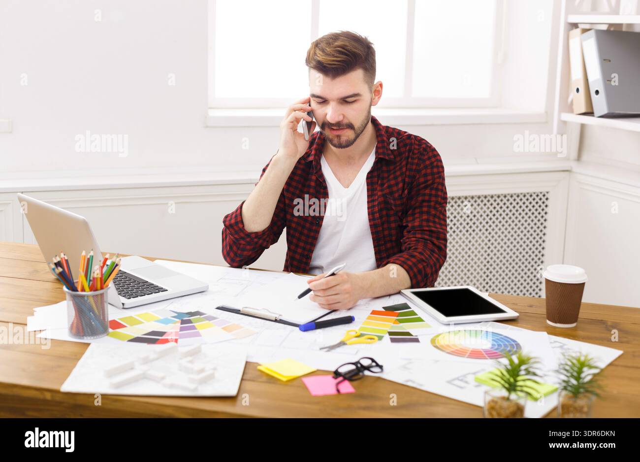 Mann, der tagsüber in einem Büro arbeitet, während er am Telefon telefoniert und zeichnet Stockfoto