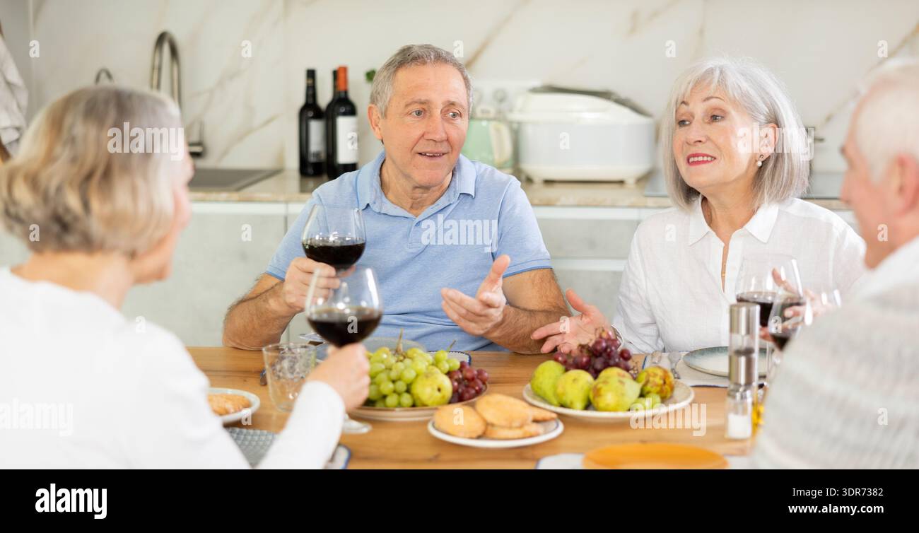 Zwei ältere Ehepaare sitzen am Tisch, genießen Essen und Wein, plaudern. Stockfoto