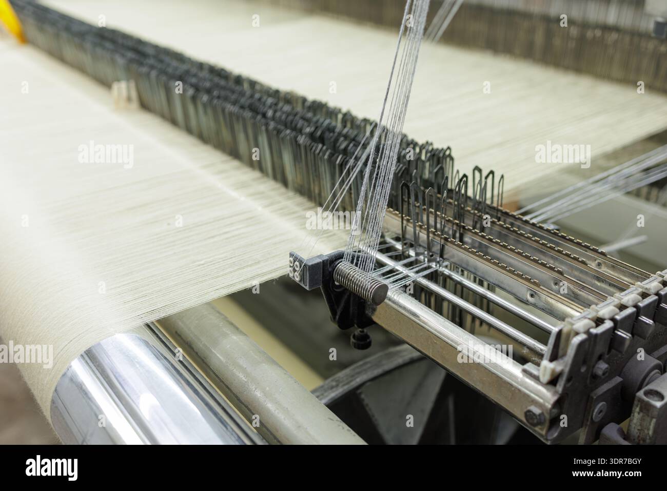 Nahaufnahme eines automatisierten Webstuhls, der Textilfäden in Stoff webt, ideal für die Herstellung, das Branding in der Textilindustrie und das Marketing in der industriellen Produktion Stockfoto