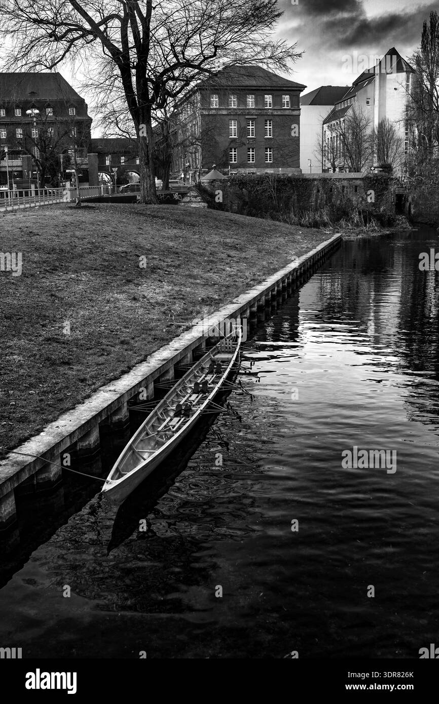 Schwarzweißfoto eines Kanals in der Altstadt mit historischen Gebäuden, die sich in ruhigem Wasser spiegeln. Starker Kontrast, führende Linien und dramatische Himmelskreation Stockfoto