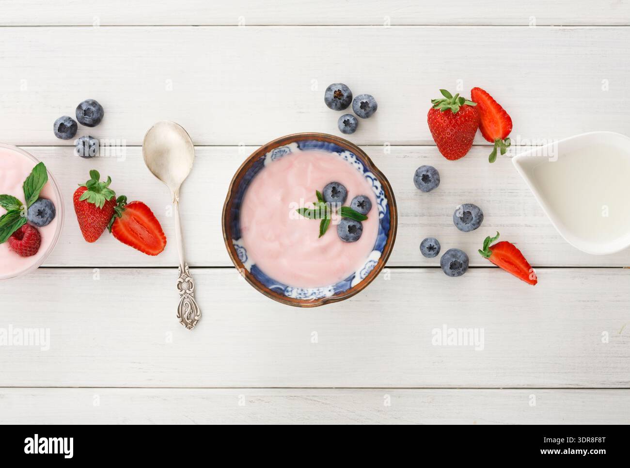 Mischung aus Obst und Joghurt auf einem Holztisch mit Löffel und Milch Stockfoto
