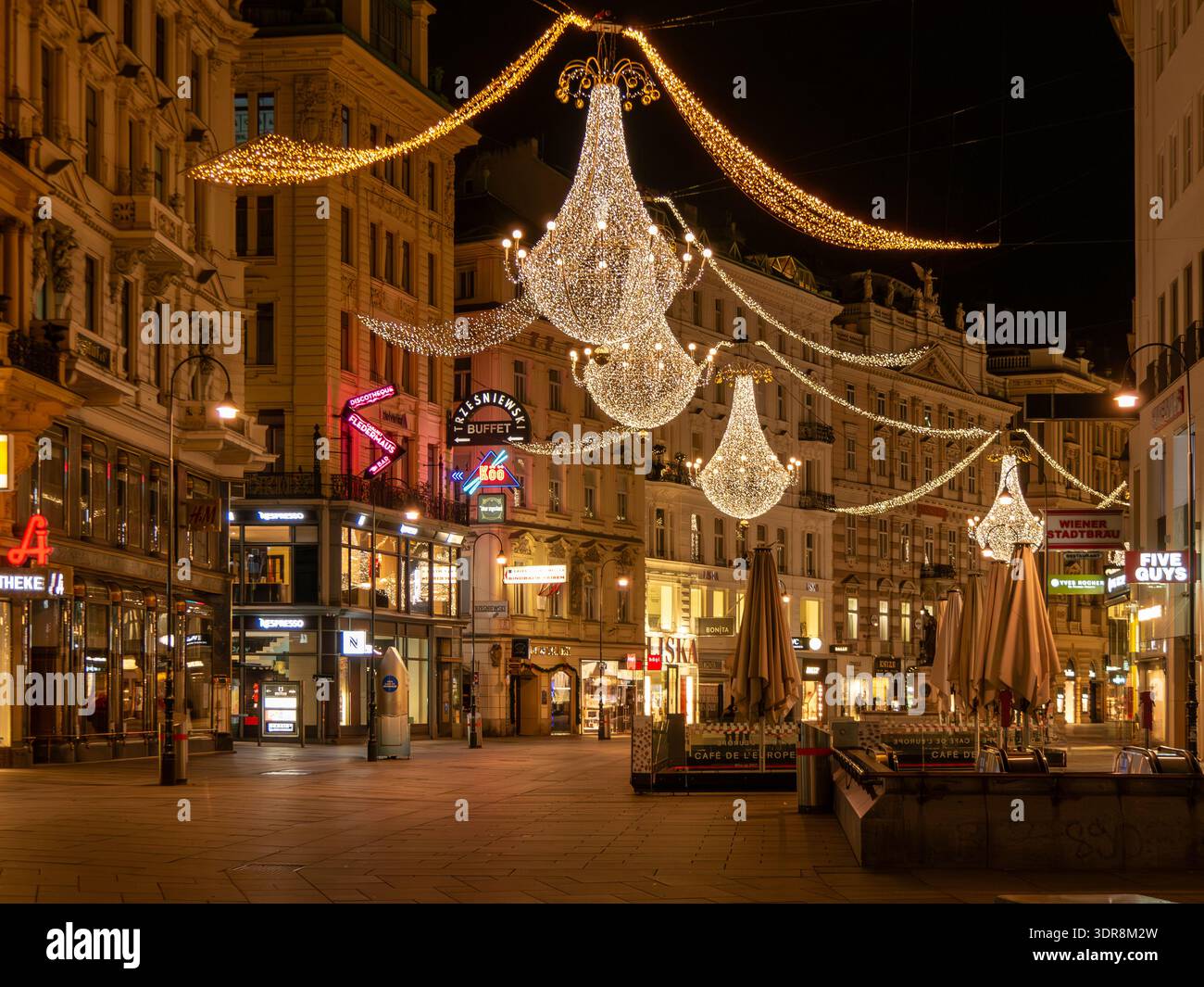 Nachtblick vom Stephansplatz zum Graben Wien: große goldene glockenförmige Weihnachtsbeleuchtung, beleuchtetes Stadtzentrum, sichtbare Markenschilder, keine Leute. Stockfoto