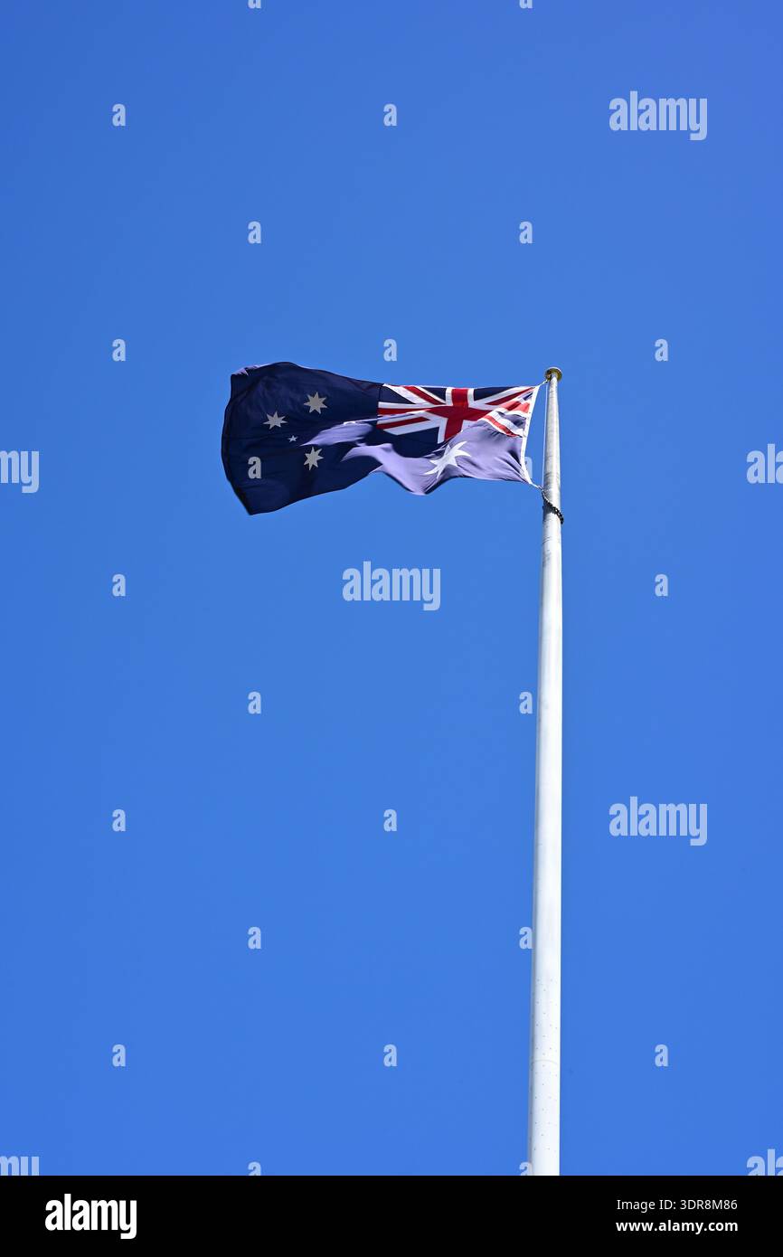 Australische Nationalflagge, die am Fahnenmast fliegt und im Wind gegen klaren blauen Himmel flattert Stockfoto