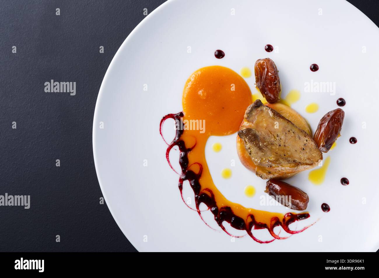 Edler Speiseteller mit Huhn, Sauce und Datteln auf schwarzer Oberfläche Stockfoto