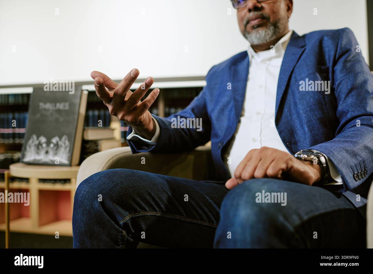 Mann mittleren Alters, der während der Präsentation des Buches in der Bibliothek Gesten gibt Stockfoto