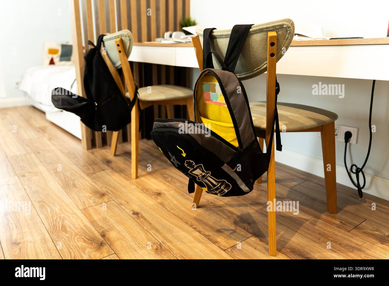 Ein Schulzimmer mit einem Schreibtisch mit Büchern für Hausaufgaben und Rucksäcken, die auf den Lehnen der Stühle hängen, in einem gemütlichen Apartment. Organisierte Studie Stockfoto