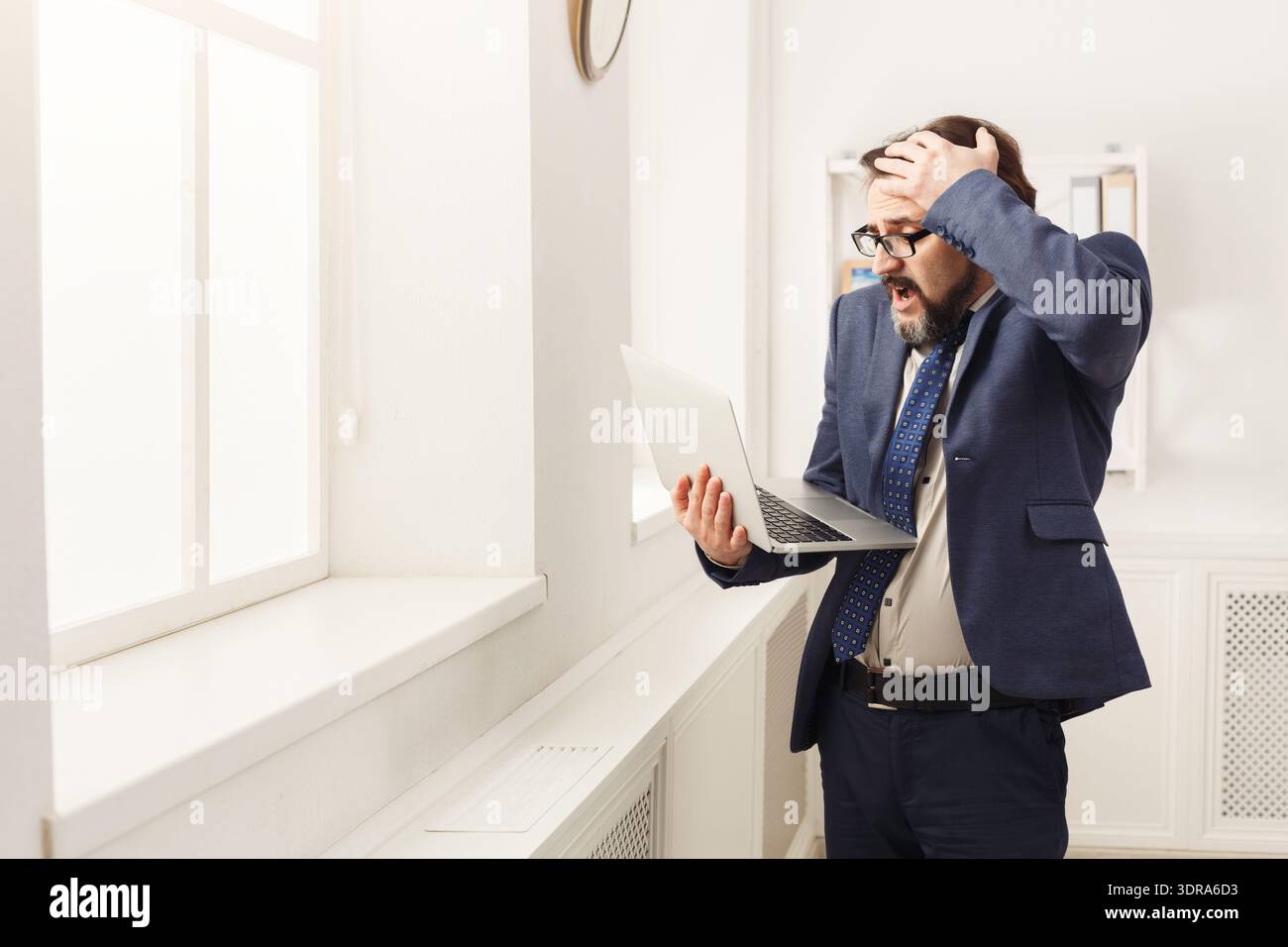 Geschäftsmann reagiert auf unerwartete Nachrichten, während er ein Notebook in einem modernen Büroumfeld verwendet Stockfoto