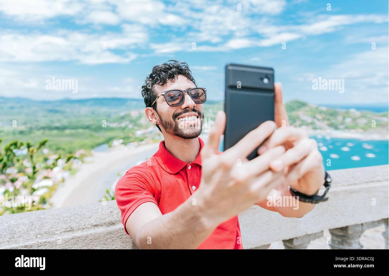 Glücklicher Tourist, der ein Selfie an einem Aussichtspunkt am Strand macht. Gutaussehender Mann, der ein Selfie am Aussichtspunkt von San Juan del Sur macht Stockfoto