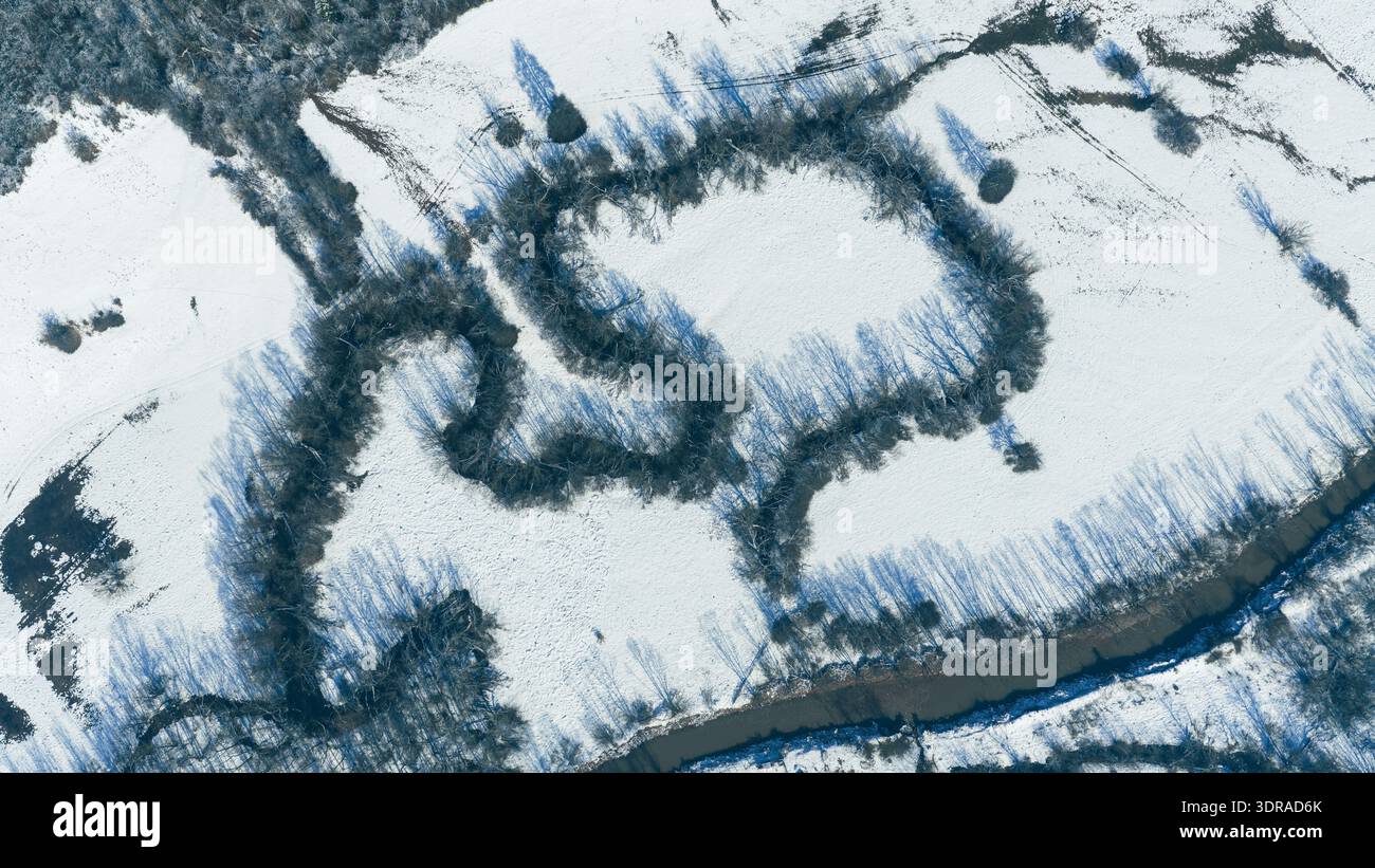 Die winterliche Landschaft mit einem sich windenden Fluss, der durch schneebedeckte Berglandschaft fließt Stockfoto