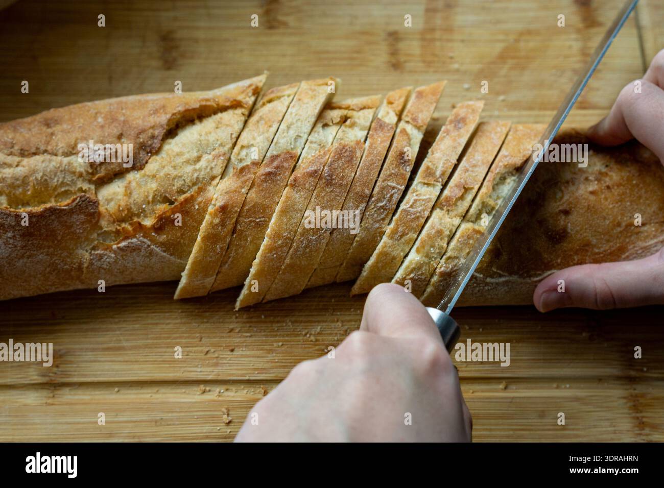 Nahaufnahme eines Baguettes, fein geschnitten auf einem hölzernen Schneidebrett. Die klare Kruste und die weiche Innenseite sorgen für einen satten Texturkontrast. Stockfoto