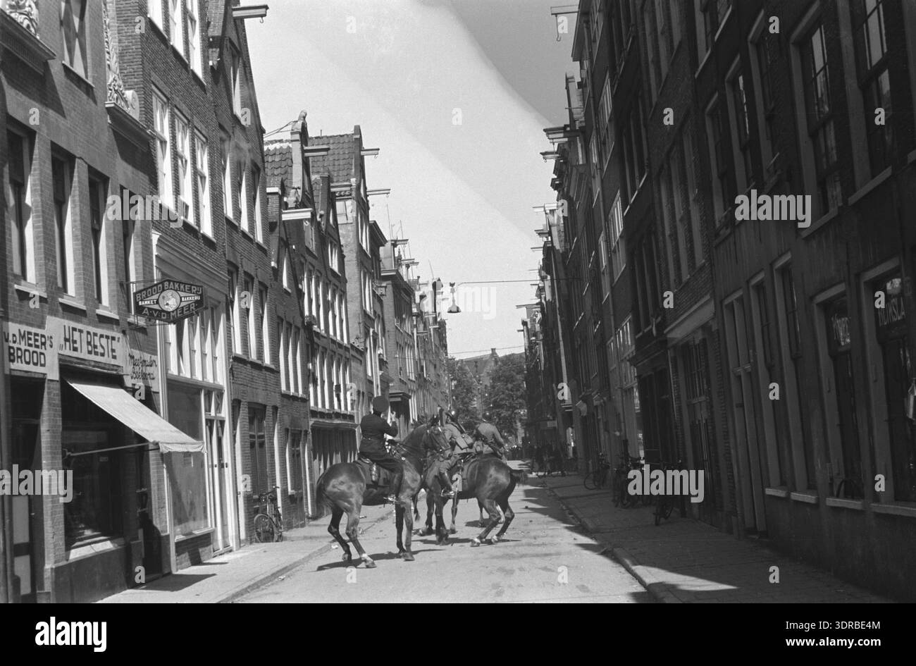 Dieses Foto zeigt den Jordaan-Aufstand in Amsterdam im Juli 1934. Soldaten und Polizisten patrouillieren zu Pferd in der Goudsbloemstraat. Das Bild erfasst die aufgehängte Strafverfolgung, das Crowdmanagement, städtische Straßenlandschaft, niederländische Bürgerunruhen, Polizeiarbeit aus dem frühen 20. Jahrhundert, und die öffentliche Ordnung während der Unruhen. Stockfoto
