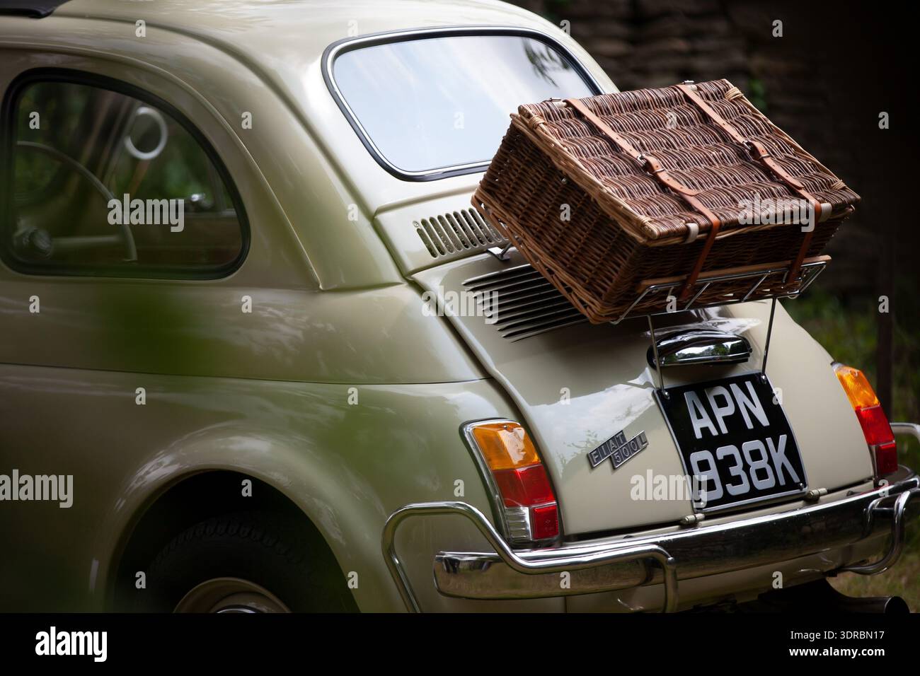 Rückansicht eines klassischen Fiat 500 mit einem Picknickkorb aus Korb auf dem Gepäckträger, im Freien geparkt, mit Vintage-Details und Chromverzierungen. Stockfoto