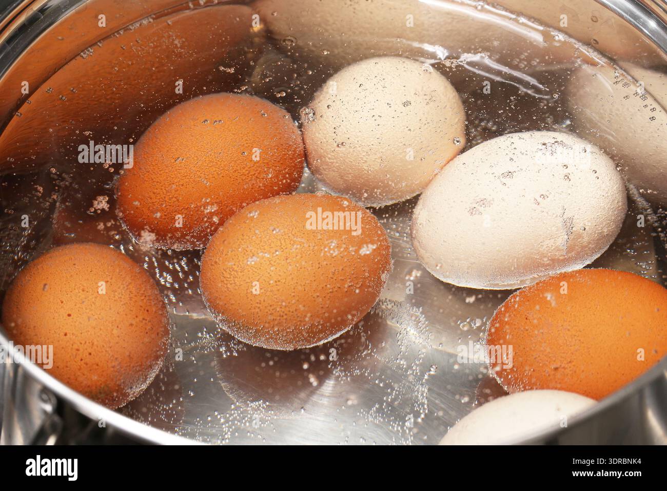 Eier kochen in heißem Wasser Nahaufnahme. Hausmannskost und Lebensmittelzubereitung in der Küche. Einfaches Alltagszutaten-Konzept. Stockfoto