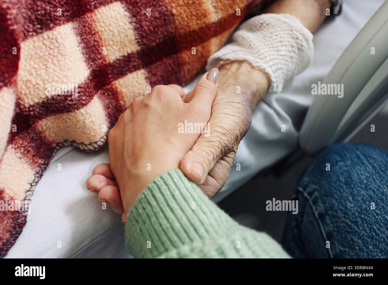 Nahaufnahme einer Frau, die die Hand eines älteren Patienten unter der Decke hält. Mitgefühl und Unterstützung bei Krankenhausbehandlung und medizinischer Versorgung im Innenbereich. Stockfoto