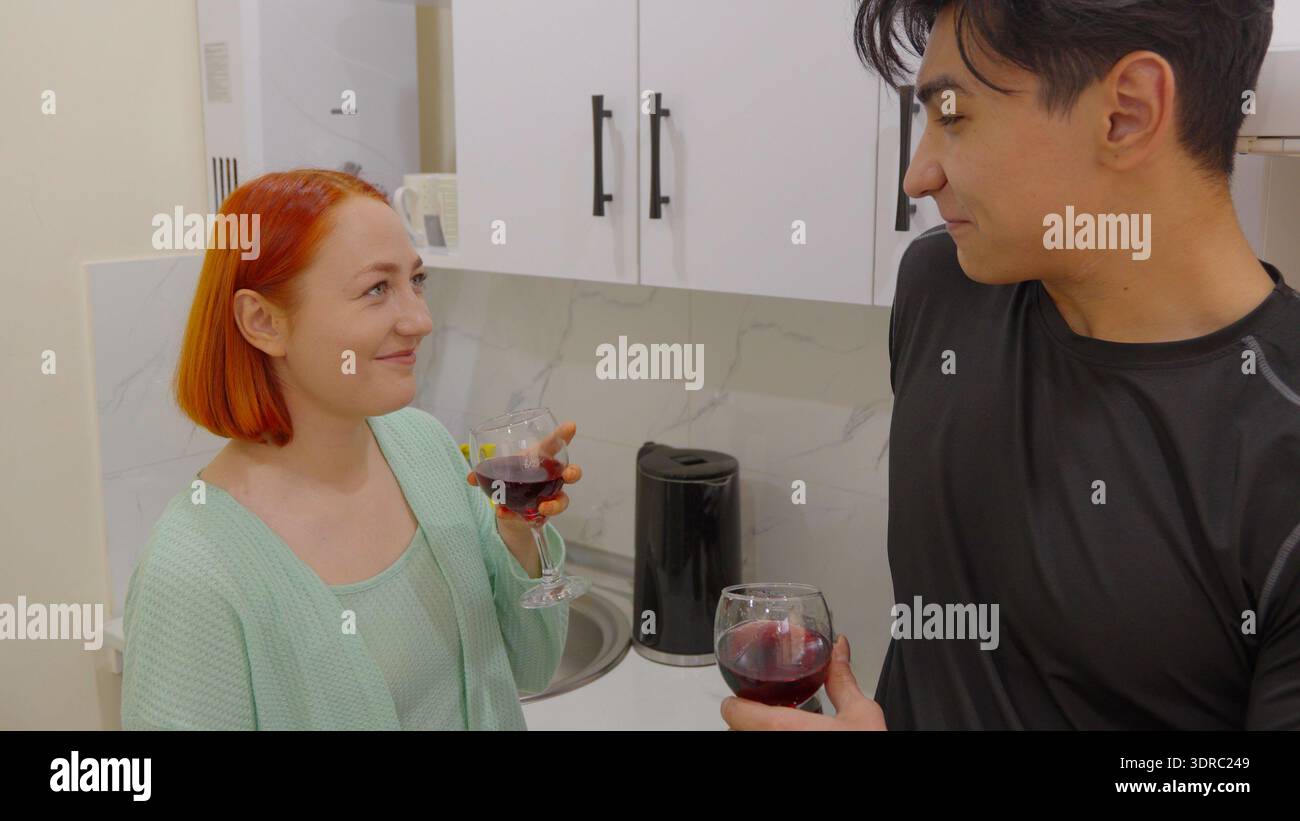 Ein junges Paar spricht und trinkt Wein in der Küche Stockfoto
