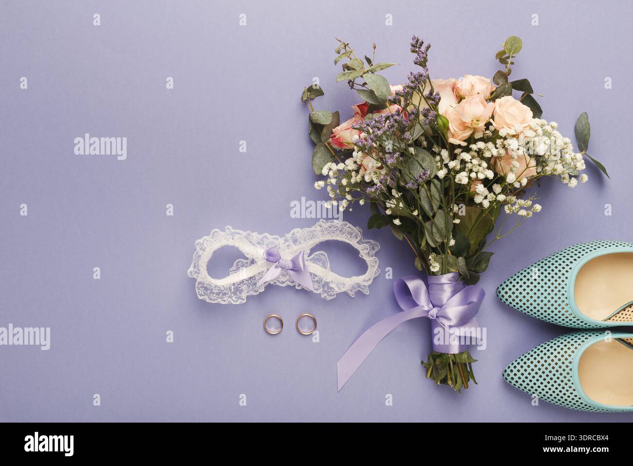 Sammlung von Hochzeitsgegenständen, einschließlich Blumen, Ringe und Schuhe, angeordnet auf einem lila Hintergrund Stockfoto