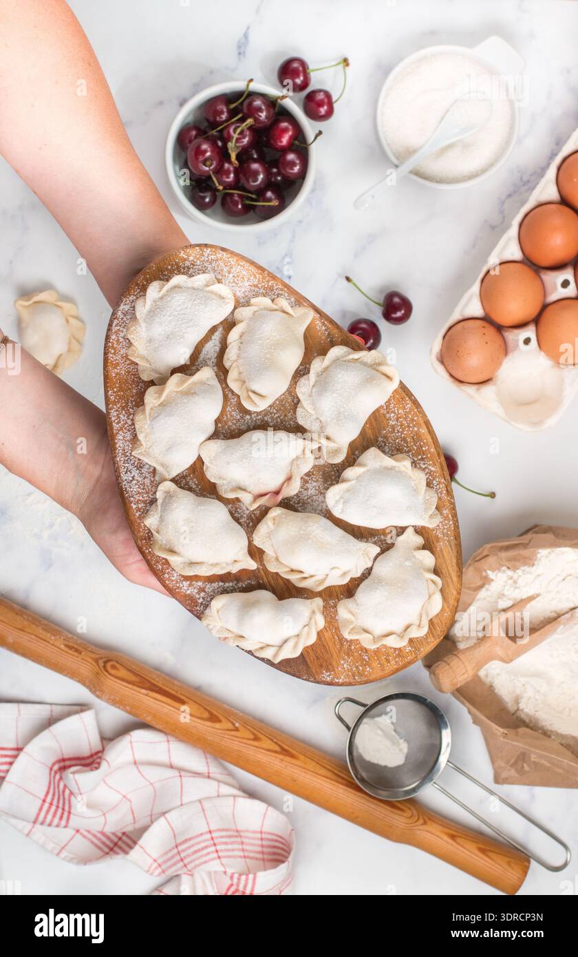 Bereiten Sie köstliche süße Teigtaschen mit Kirschen zu. Traditionelles russisches und ukrainisches Dessert. Vareniki und Zutaten auf dem Merb Stockfoto