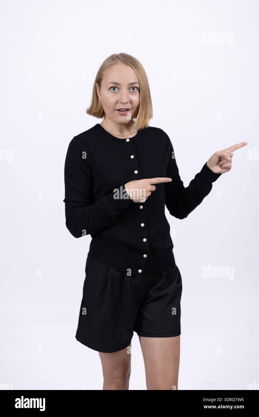 Eine junge Frau in schwarzem Kleid, die im Studio zur Seite zeigt Stockfoto
