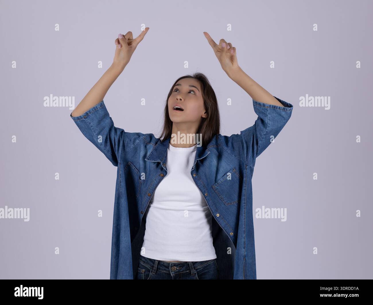 Junge Frau in blauem Hemd, die mit beiden Händen nach oben zeigt Stockfoto