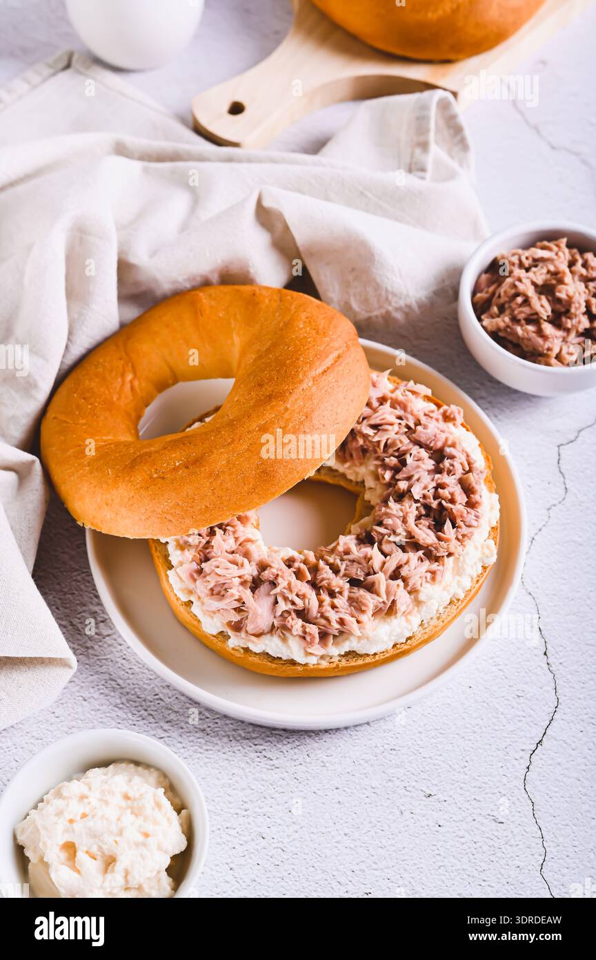 Herzhafter Bagel Burger mit Thunfisch und Ricotta auf einem Teller auf dem Tisch, vertikale Ansicht Stockfoto