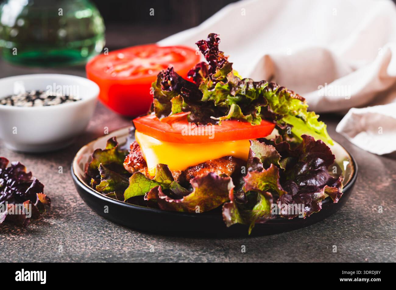 Scharfer Keto Burger auf frischen Salatblättern von Schnitzel, Tomaten und Käse auf einem Teller auf dem Tisch Stockfoto