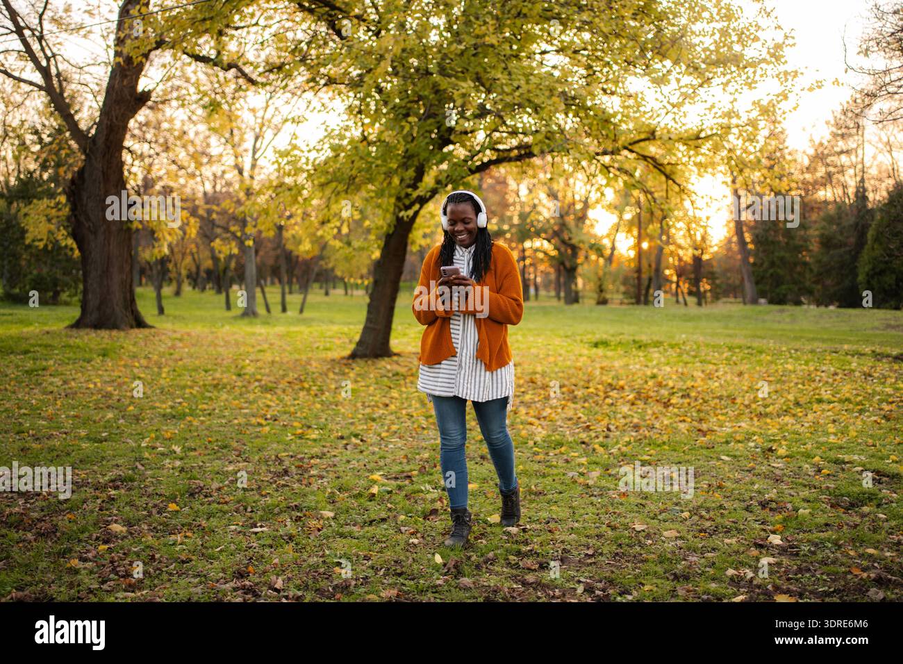 Junge Frau, die Musik über Kopfhörer im Herbstpark genießt Stockfoto