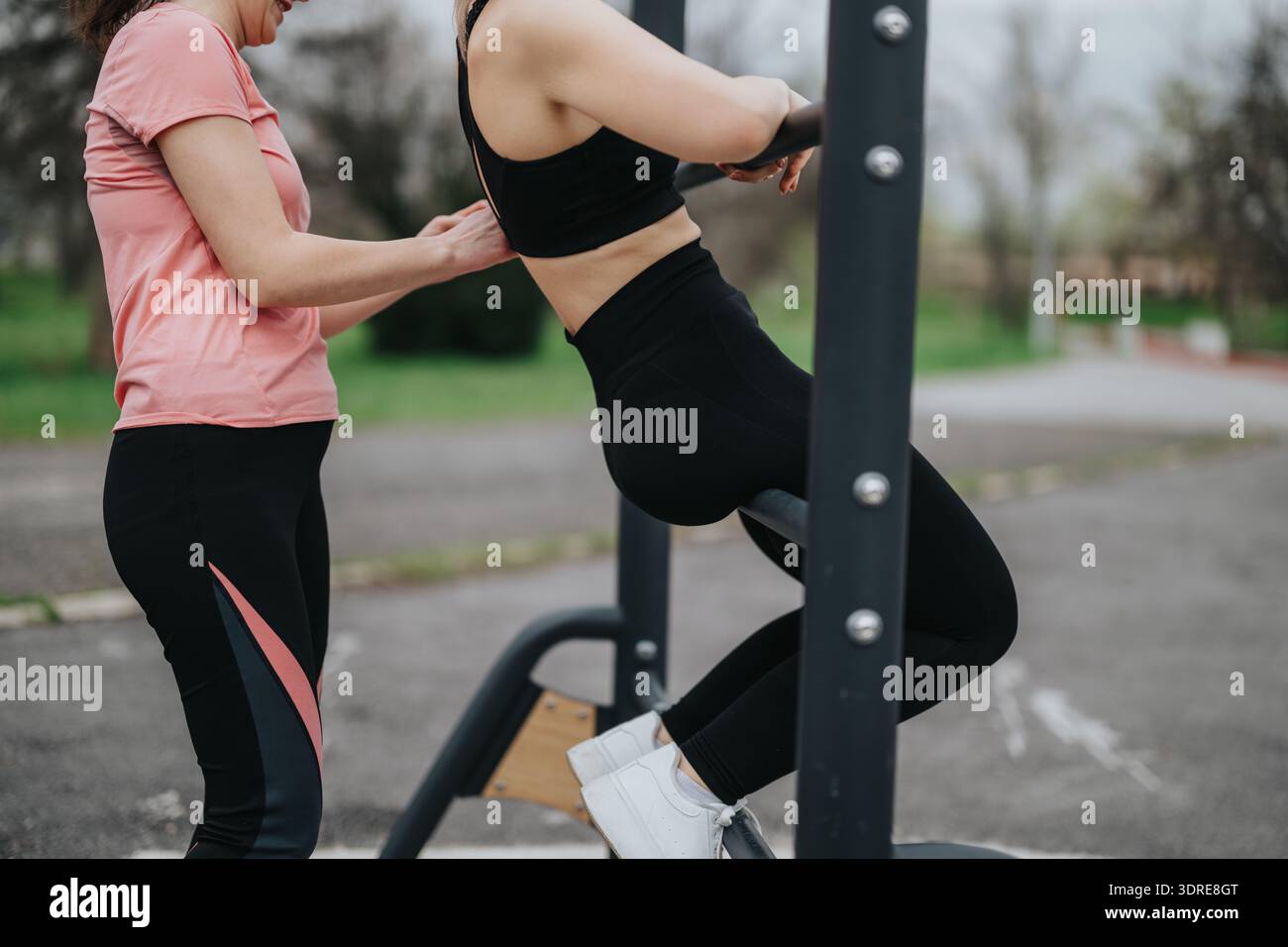 Frau erhält Unterstützung beim Training im Freien, da sie heute ein strukturiertes Fitnessgerät benutzt Stockfoto