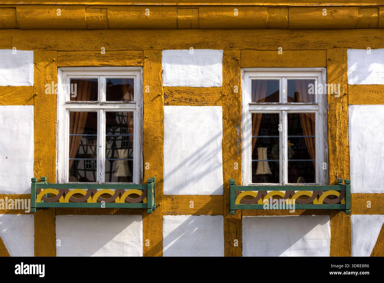 Zwei Fenster in der Fassade eines alten Fachwerkhauses mit Blumenkasten und gelb getönten Holzbalken Stockfoto