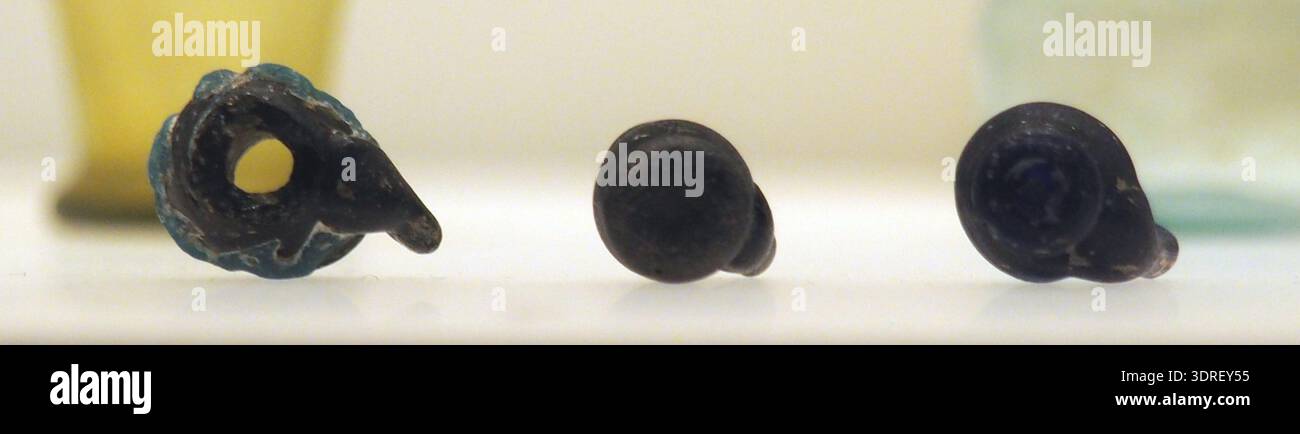 Bild von drei vasenförmigen Perlen MF 3666, MF 3667, MF 3668 aus dem 4. Jahrhundert, die Form, Perforation und Material für das Fadenziehen hervorheben. Diese dekorativen Artefakte veranschaulichen spätantike persönliche Verzierungen und rituelle Praktiken. Das Foto dokumentiert Typologie, Handwerkskunst und Design und unterstützt die archäologische Analyse der materiellen Kultur, des Handels und des stilistischen Ausdrucks in der Zeit. Perlen sind Belege für die Verwendung kleiner Artefakte in kulturellen, persönlichen und zeremoniellen Kontexten. Stockfoto