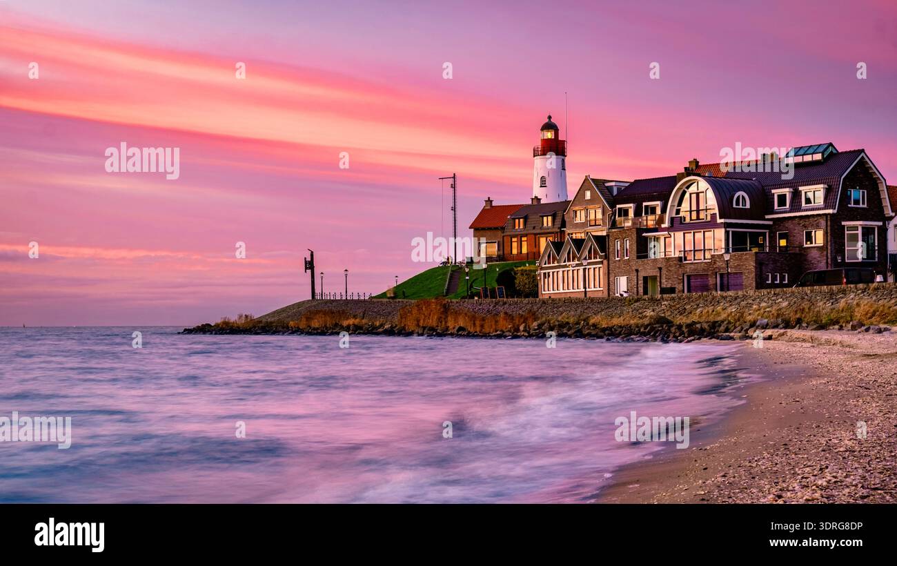 Farbenfroher Sonnenuntergang über einem Küstendorf mit einem Leuchtturm und ruhigen Meereswellen Stockfoto