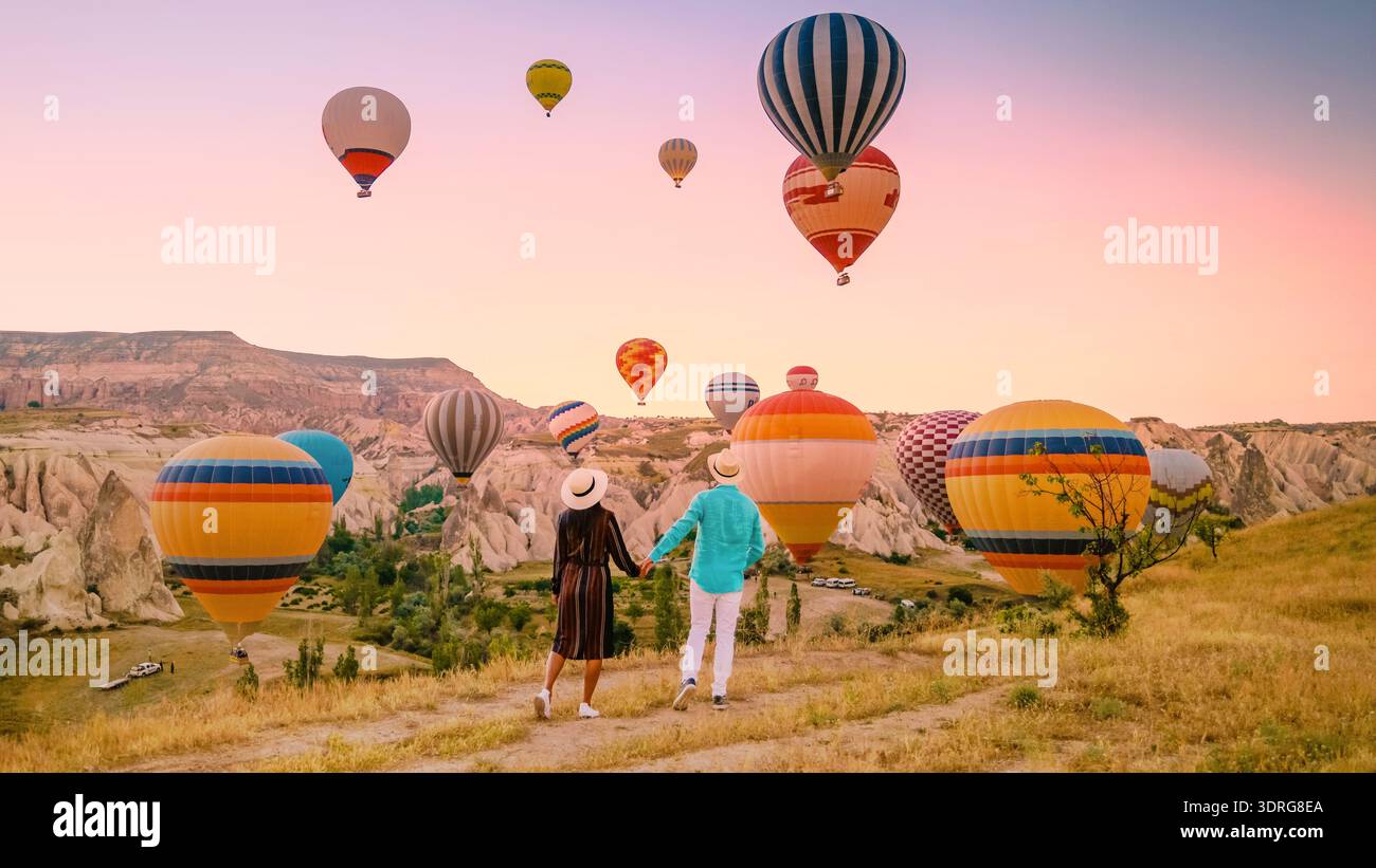 Ein Paar erlebt einen magischen Sonnenaufgang in Kappadokien mit Heißluftballons, die über ihnen schweben Stockfoto