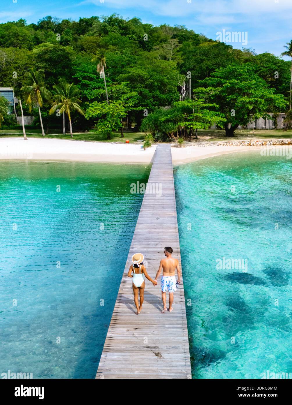 Ein paar Spaziergänge entlang eines malerischen hölzernen Piers, umgeben von kristallklarem türkisfarbenem Wasser und üppigem tropischem Grün der Insel Koh Kham in der Nähe von Koh Mak T Stockfoto
