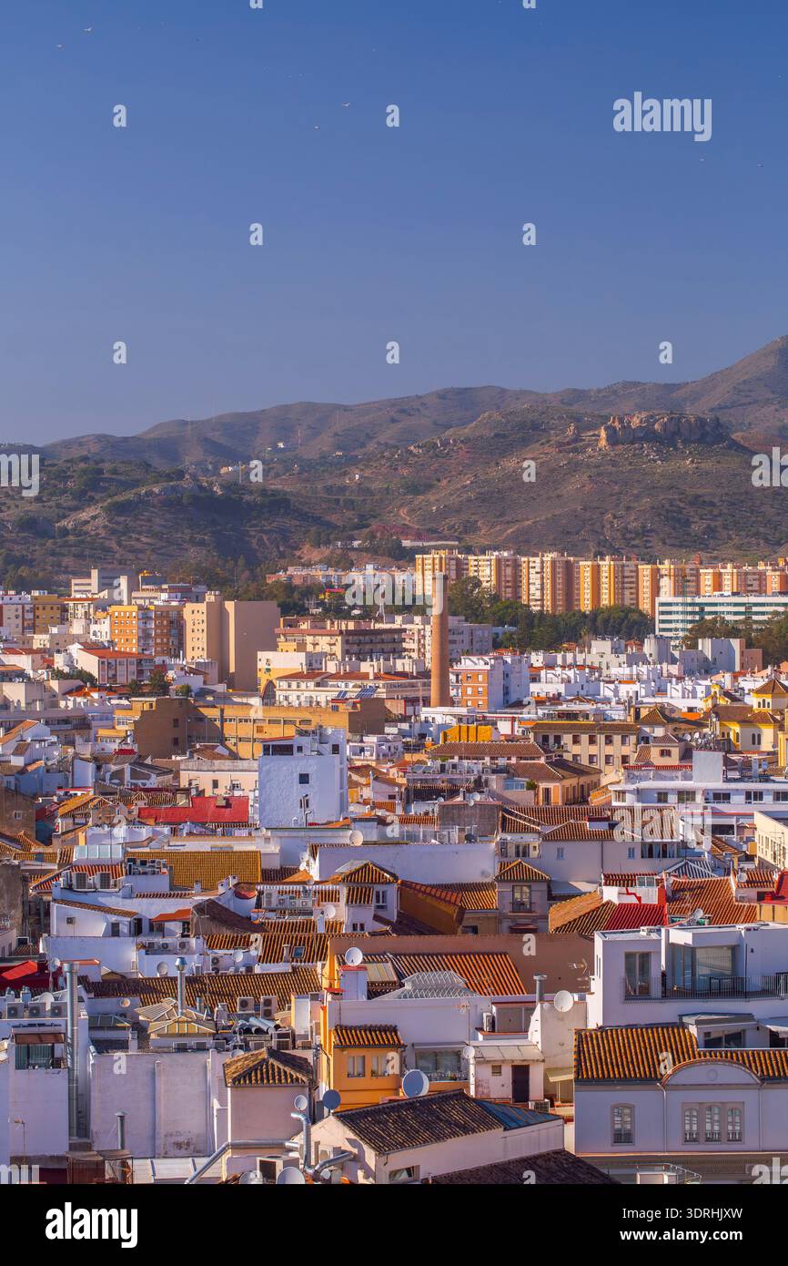 Malaga, Spanien. Dichte städtische Dächer und ein historischer Industrieschornstein mit Bergen in der Ferne. Traditionelle mediterrane Stadtarchitektur und Stockfoto