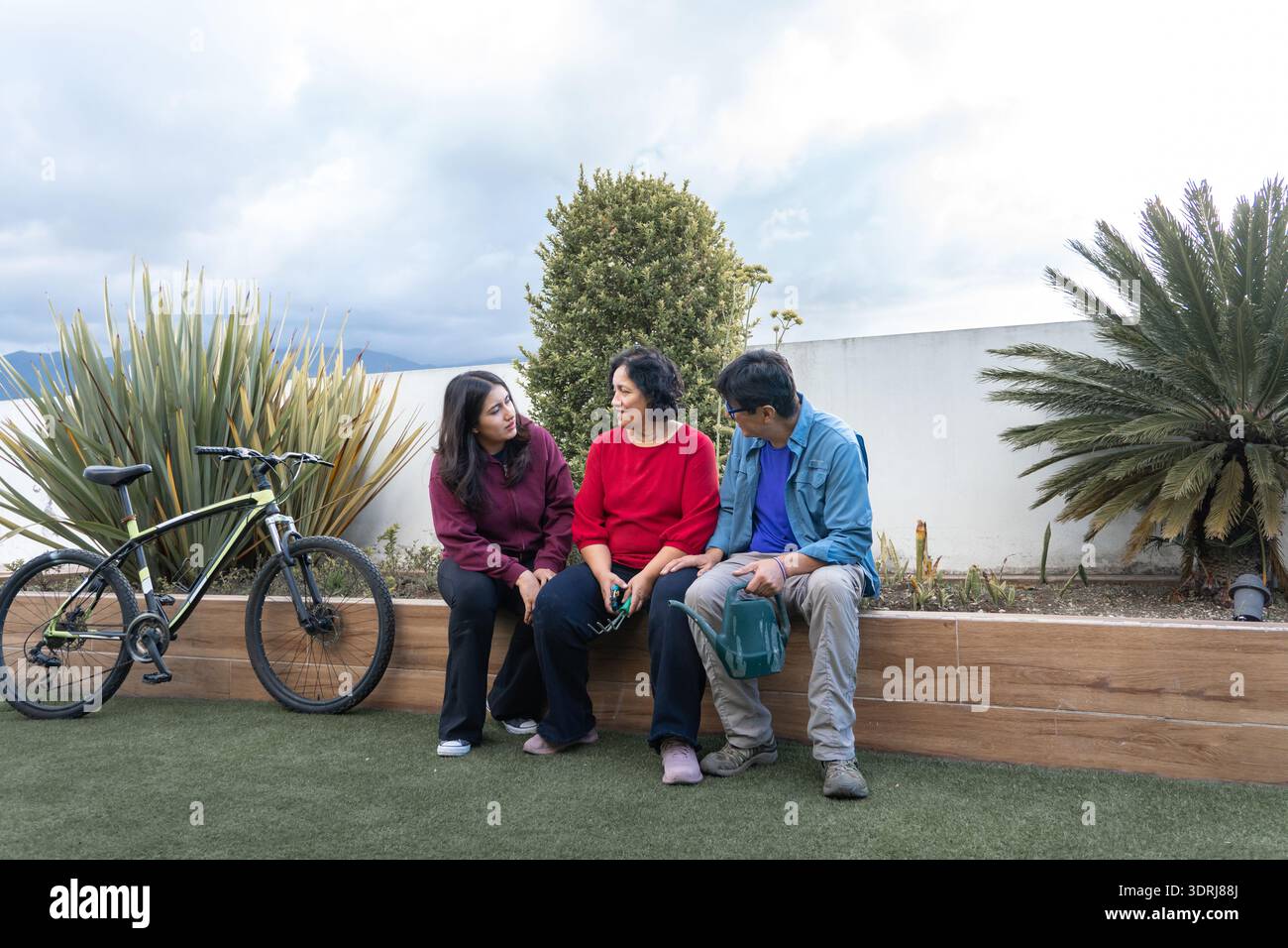 Familienmitglieder sitzen und unterhalten sich draußen auf einer Terrasse mit Fahrrad Stockfoto