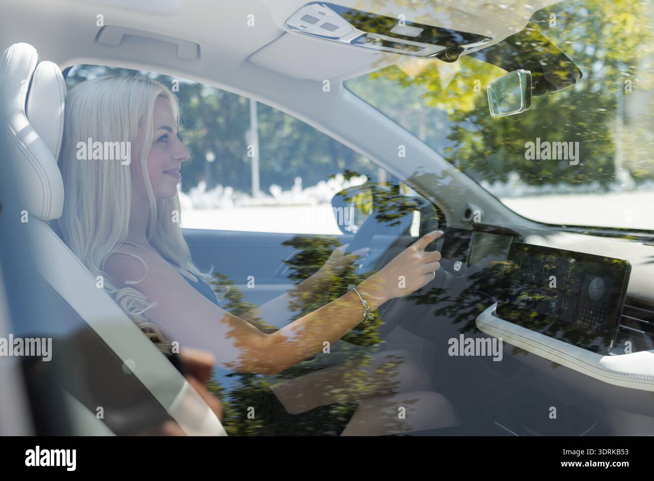 Eine Frau sitzt in einem Auto und hält das Lenkrad, während sie nach vorne blickt. Die Sonne scheint durch die Fenster mit Reflexionen. Stockfoto