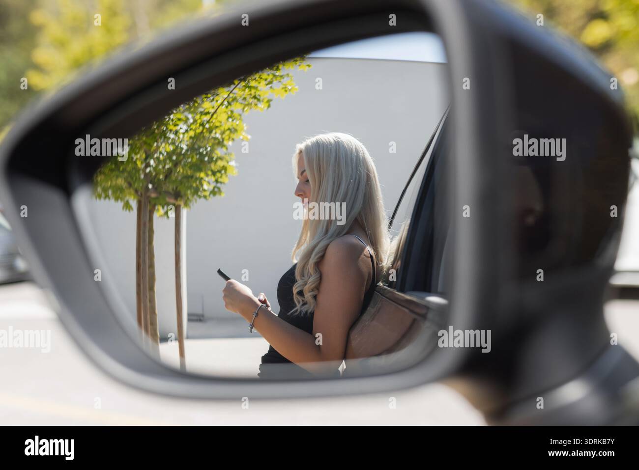 Eine Frau sitzt in einem geparkten Auto und schaut bei Tageslicht auf ihr Telefon draußen auf einem Parkplatz. Stockfoto