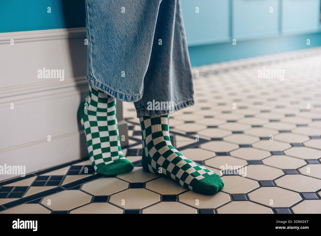 Individuelle, grün-weiß karierte Socken stehen auf gemustertem Fliesenboden und bieten lässige Mode und Komfort Stockfoto