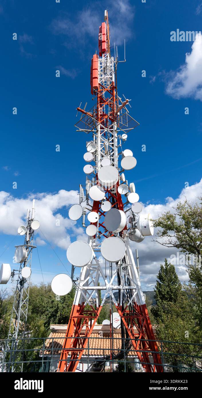 Niedrigwinkelansicht eines rot-weißen Telekommunikationsturms mit mehreren Antennenschüsseln und Geräten, fotografiert unter einem hellblauen Himmel in Andalus Stockfoto