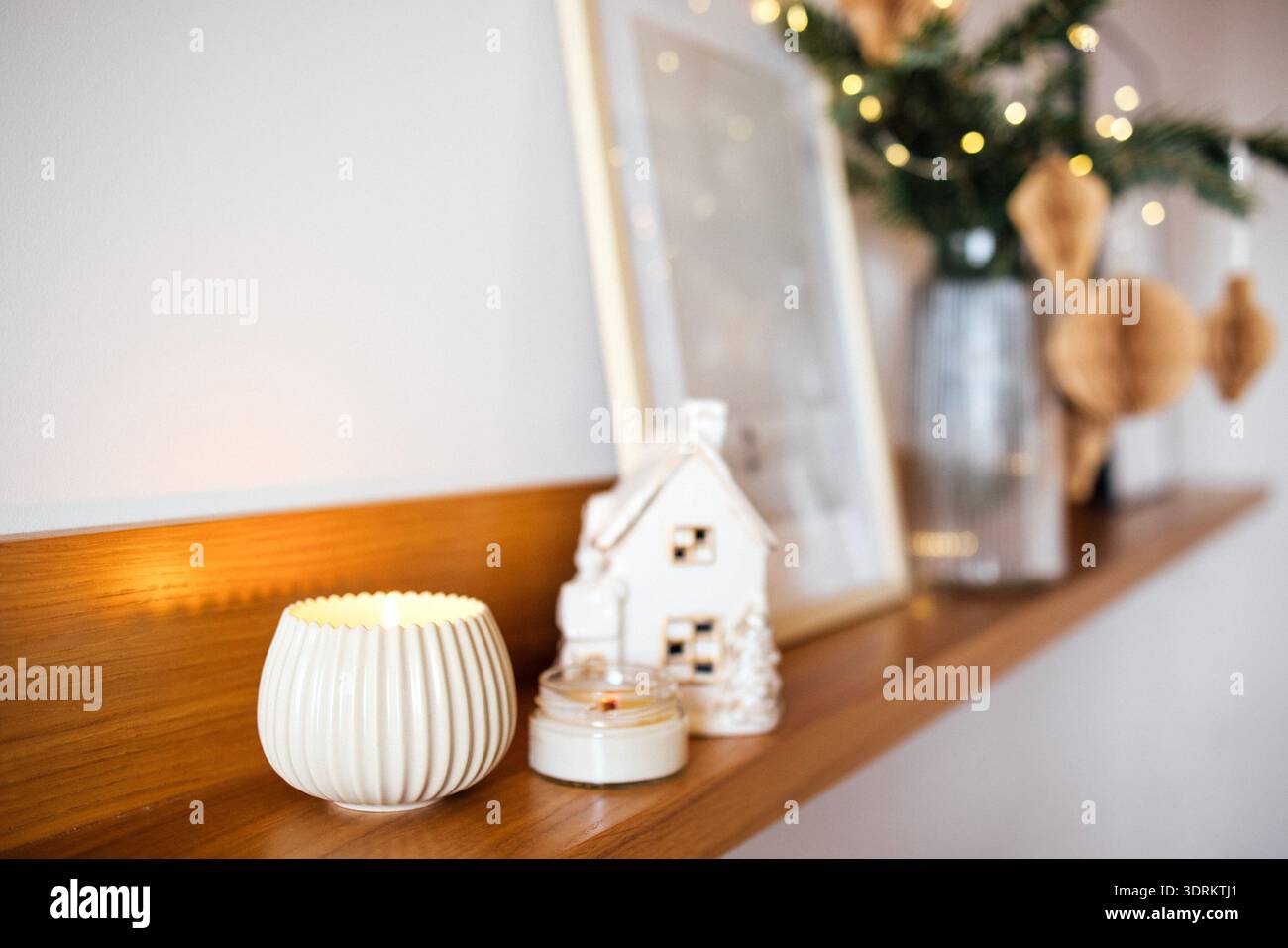 Gemütliches Innenleben mit dekorativer Kerze, einem kleinen Keramikhaus und einem gerahmten Bild auf einem Holzregal, was einen Krieg verursacht Stockfoto