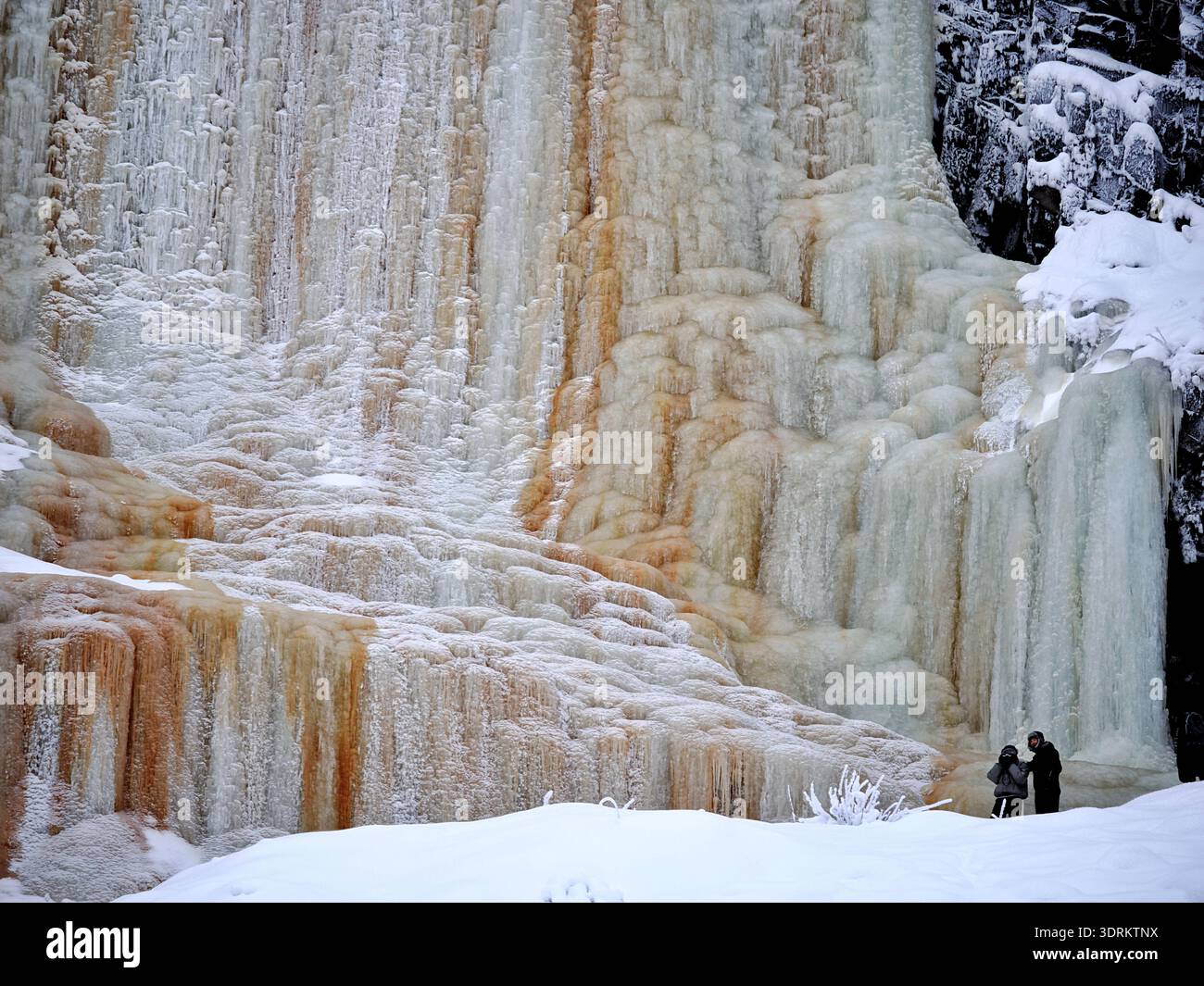 Ein junges Paar posiert für Fotos am Boden eines riesigen gefrorenen Wasserfalls, Korouoma Canyon, Finnland Stockfoto
