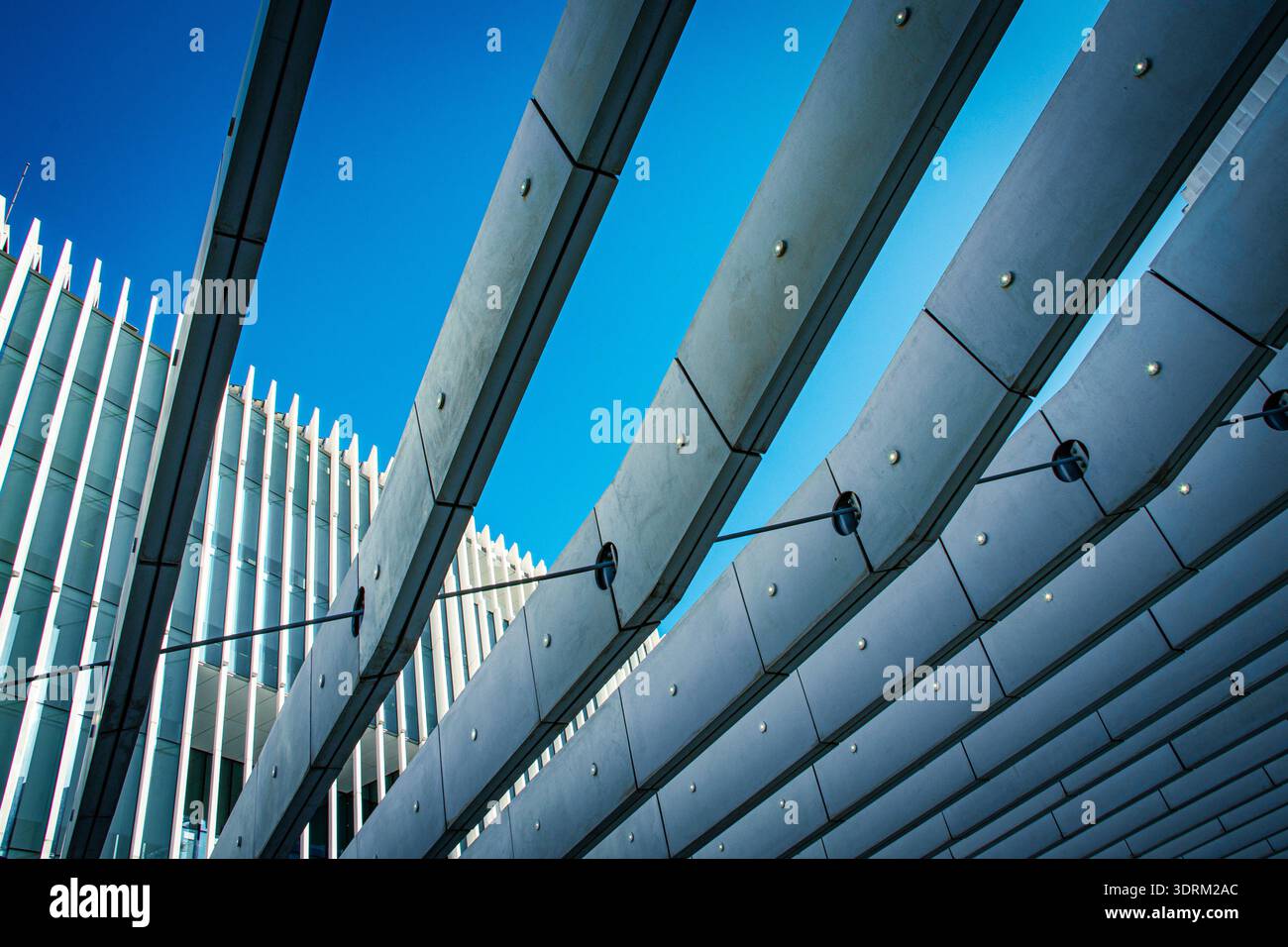 Dynamischer Blick auf zeitgenössische Architektur mit schwungvollen Betonbalken und Stahlstützen vor einem leuchtend blauen Himmel. Lissabon. Stockfoto