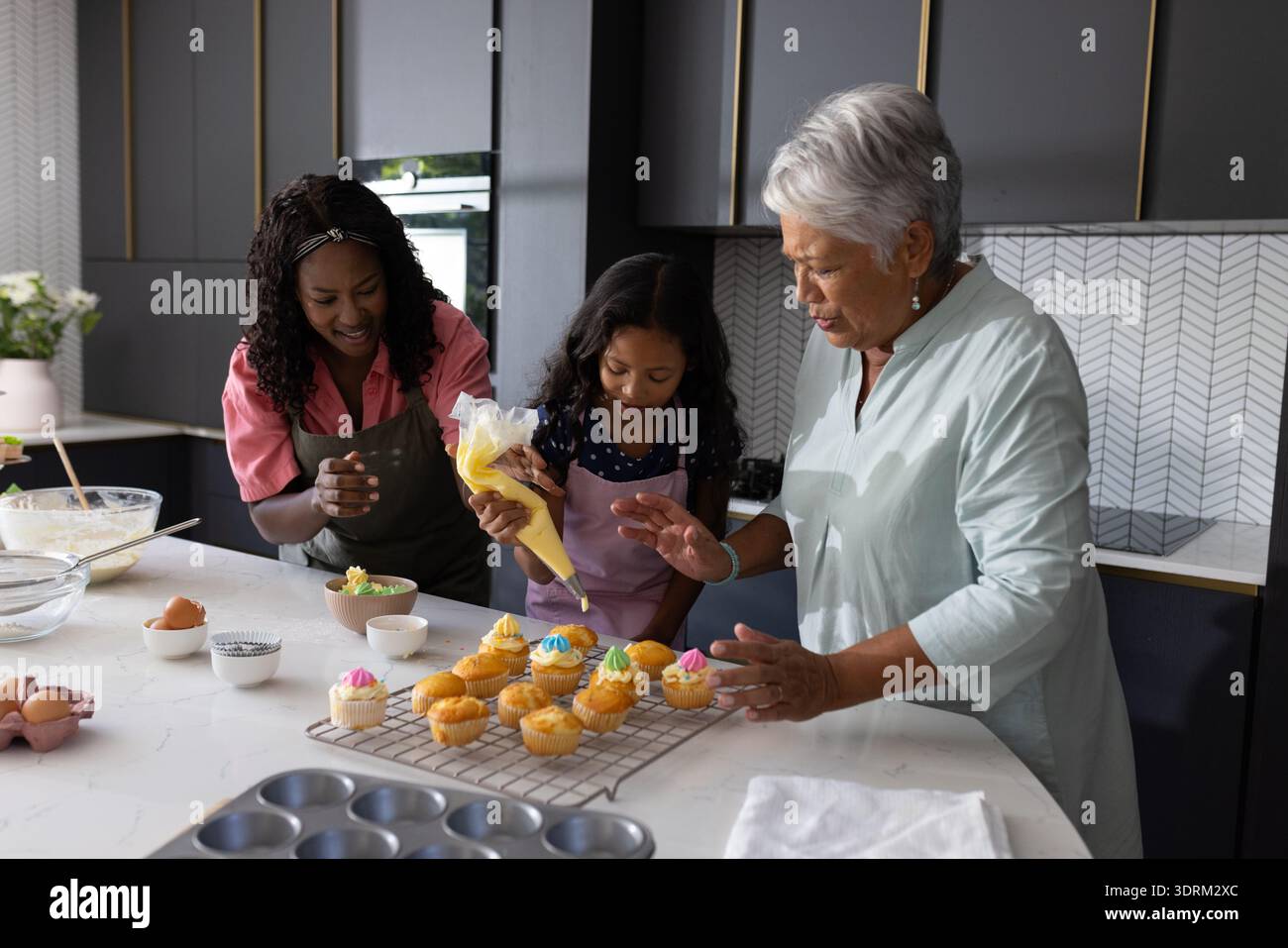 Die Dekoration von Cupcakes in der modernen Küche, drei Generationen, die fröhliche Momente miteinander teilen. Familie, Binden, Backen, Kulinarik, des Stockfoto