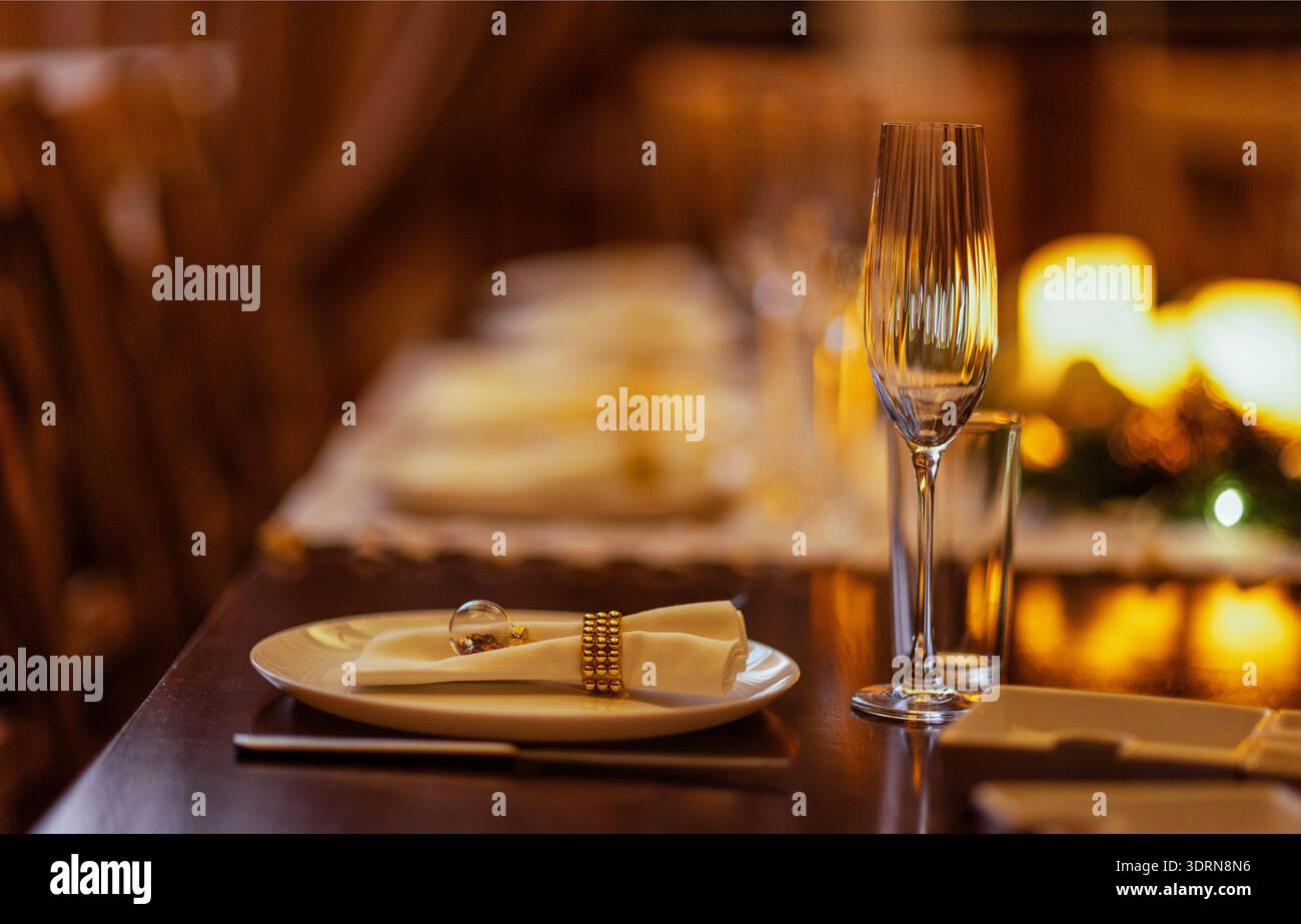 Eleganter Esstisch mit weißen Tellern, glitzernden Gläsern und dekorativen Servietten für eine warme und einladende Atmosphäre Stockfoto