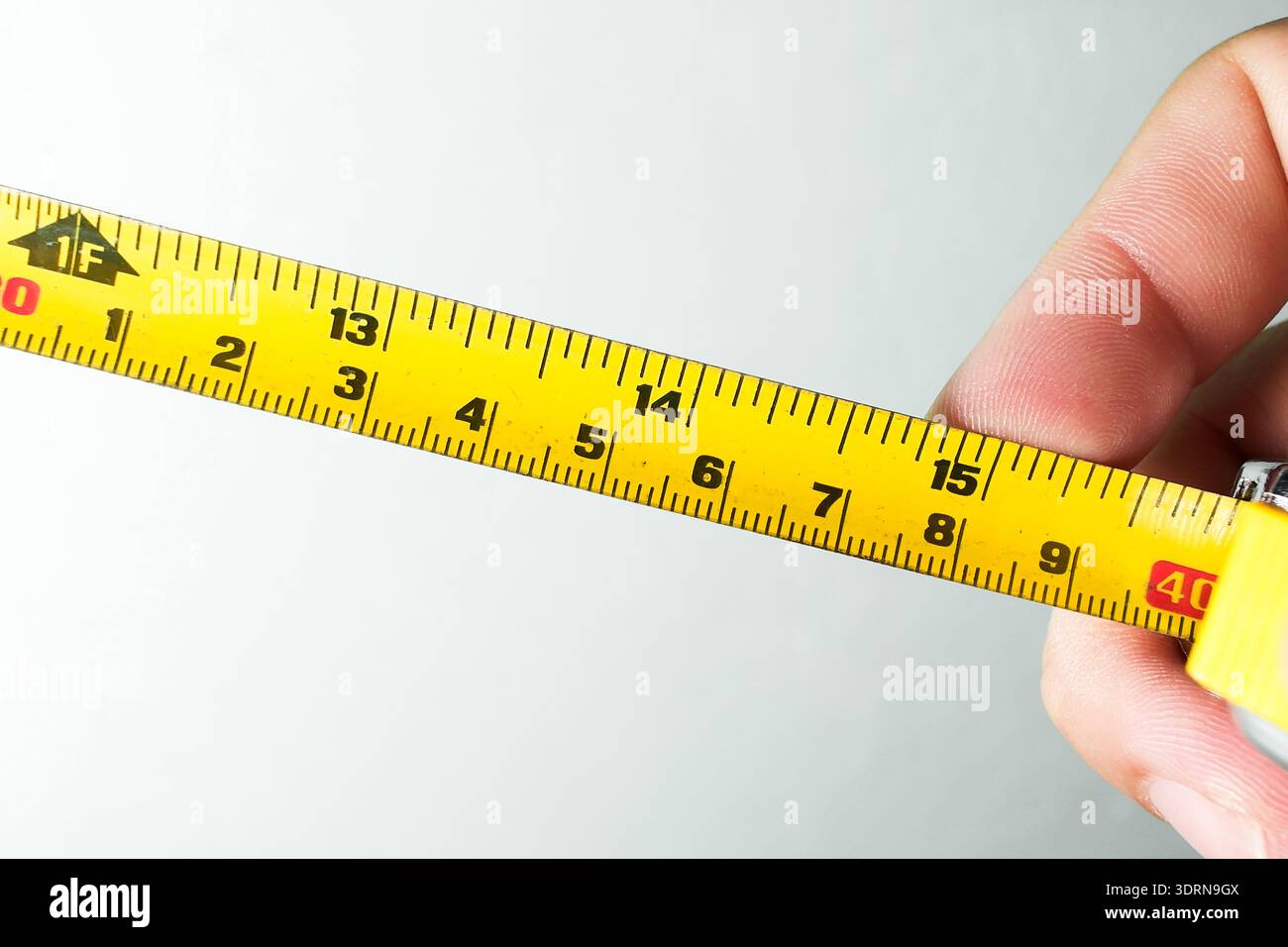 Präzisions-Messgeräte: Eine Hand hält ein gelbes, einziehbares Maßband, das Markierungen in Zoll und Zentimetern zeigt. Stockfoto