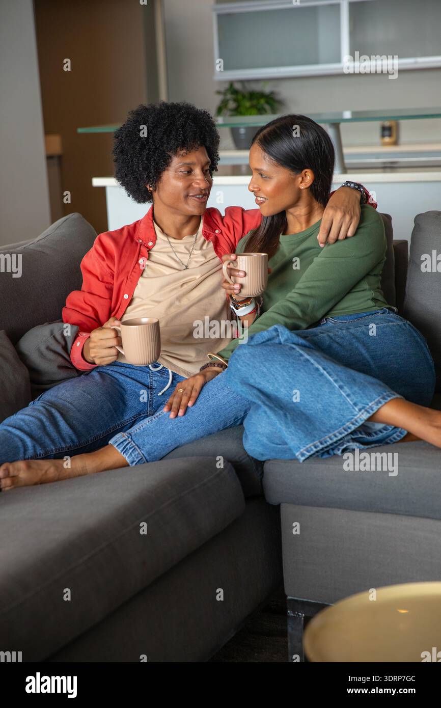Verschiedene Paare sitzen auf einem grauen Sofa im Wohnzimmer und halten Keramikbecher mit Küchenpflanzen. Intimität, Entspannung, modern, gemütlich, Stockfoto