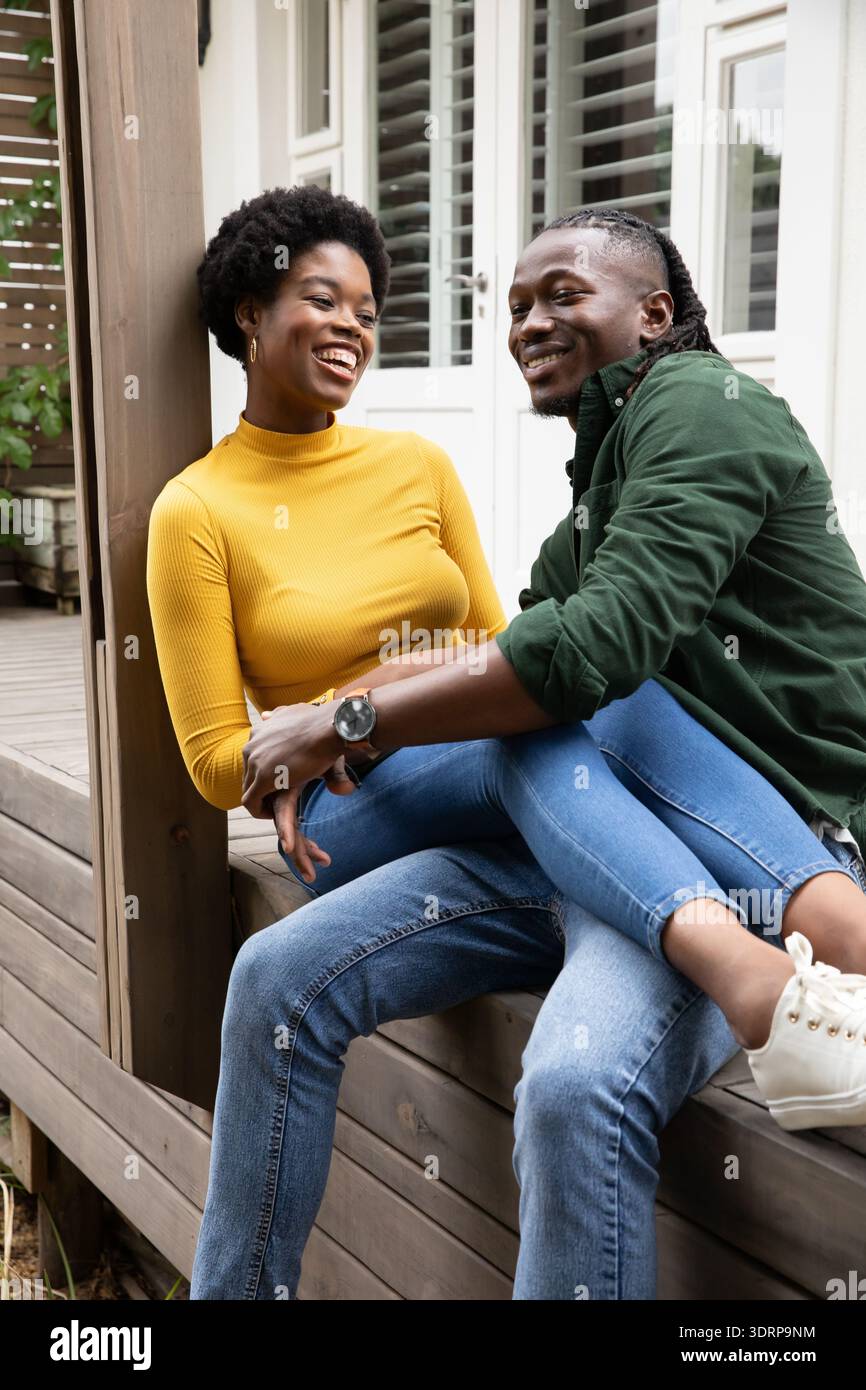 Afroamerikanisches Paar sitzt dicht und lächelt auf einer Veranda mit Fensterlächen. Romantisch, Freizeit, Lifestyle, gemütlich, autonom Stockfoto