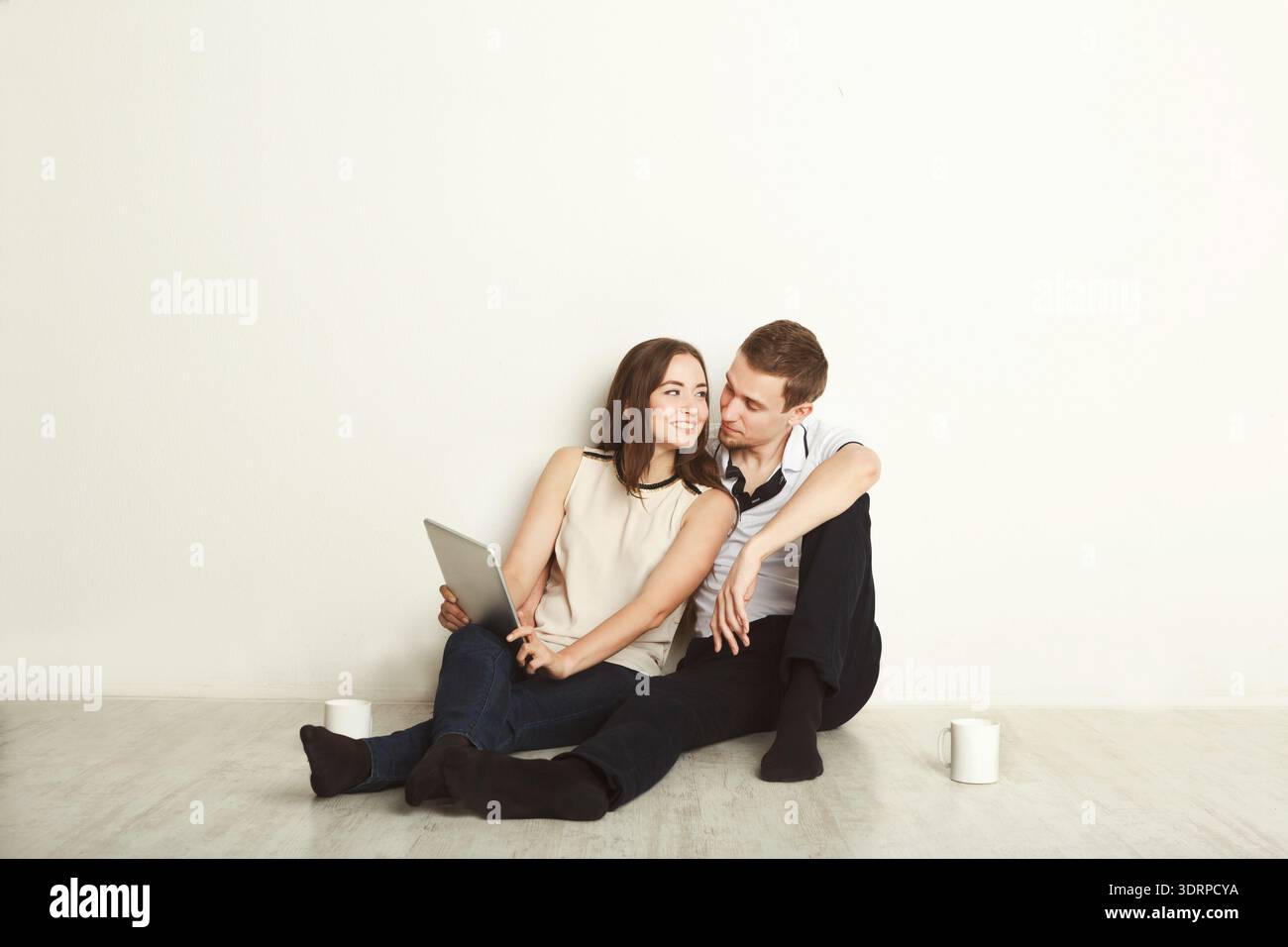 Das Paar sitzt zusammen und teilt einen Moment, während Sie ein Tablet in einer einfachen Innenumgebung verwenden Stockfoto