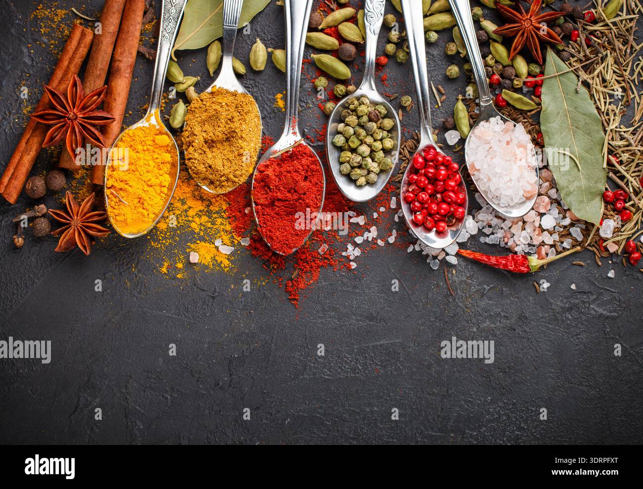 Vielfalt an natürlichen Gewürzen, Gewürzen und Kräutern in Löffeln auf dem Steintisch - Paprika, Curry, Koriander, Kardamom, Kurkuma, RO Stockfoto
