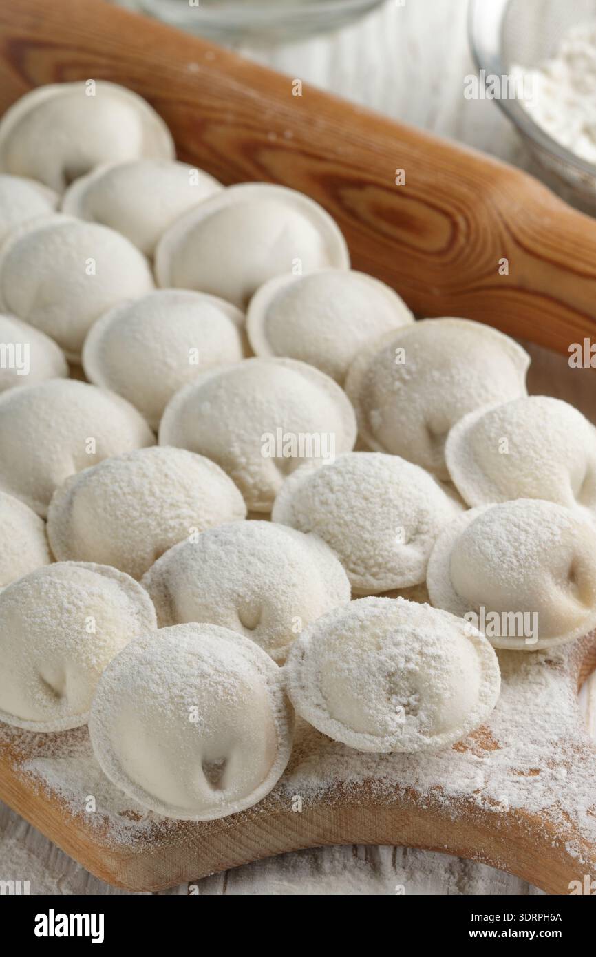 Verfahren zur Herstellung hausgemachter roher Teigklöße mit Fleischfüllung auf einem Holzbrett. Pelmeni. Ein traditionelles Gericht mit russischem Cuis Stockfoto